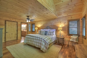 A wooden cabin bedroom with a bed, a nightstand, a chair, and a ceiling fan.