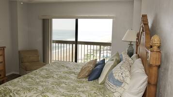 A bedroom with a large bed, a chair, a nightstand, and a view of the ocean.