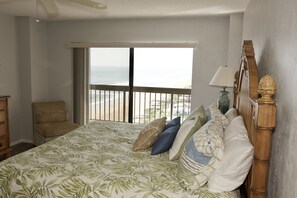 A bedroom with a large bed, a chair, a nightstand, and a view of the ocean.