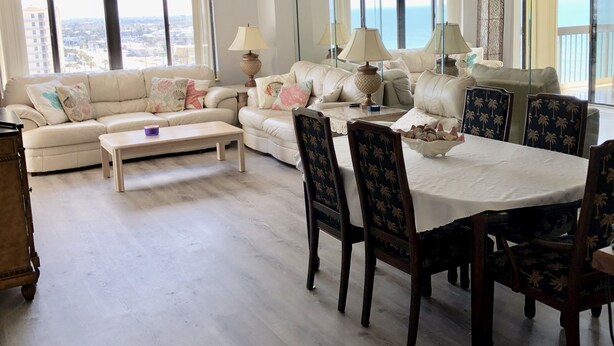 Amplia sala de estar con un conjunto de sofás, una mesa de comedor con sillas y vista al océano a través de amplias ventanas.