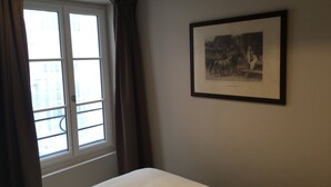 Une pièce avec un lit, une fenêtre avec des rideaux et un tableau encadré au mur.
