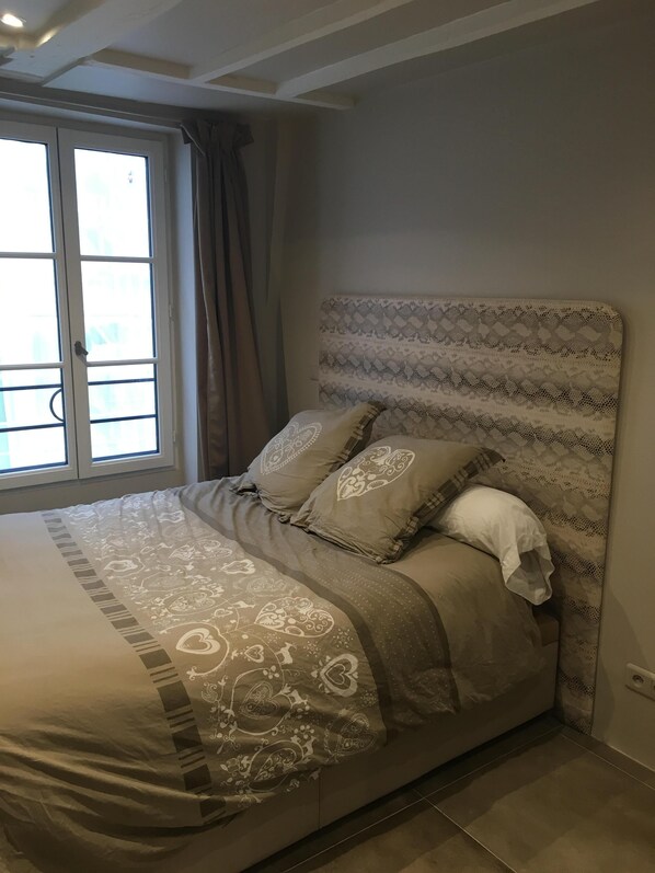A bedroom with a bed, patterned headboard, and a window with curtains.