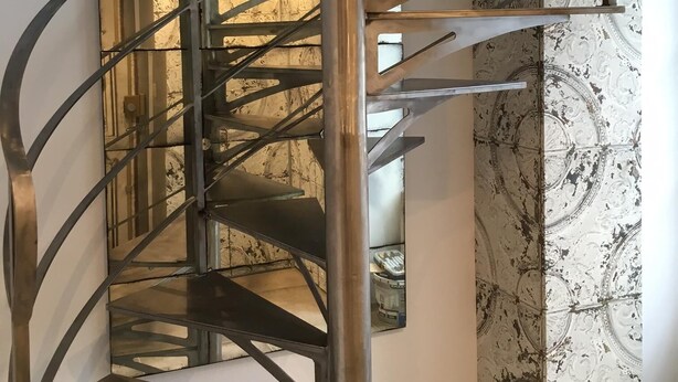 Un escalier en colimaçon avec des rampes en métal et un mur à motifs en arrière-plan.
