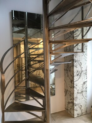 A spiral staircase with metal railings and a patterned wall in the background.