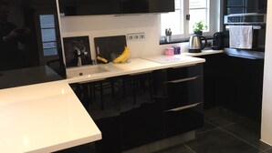 Une cuisine moderne avec des meubles noirs, un plan de travail blanc, un évier, une cuisinière et une fenêtre agrémentée de plantes.