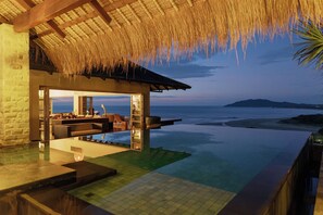 A infinity pool with a view of the ocean, a thatched roof structure, and a lounge area with seating and a table. - Casa Alang Alang - majestic ocean views by Elite Beach Villas (Tamarindo)