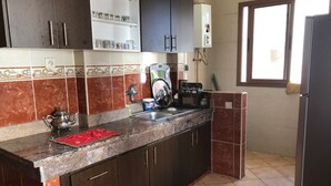 Une cuisine avec des meubles en bois foncé, un plan de travail en marbre, une machine à café et une fenêtre avec des stores.