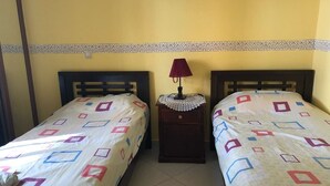 Une chambre avec deux lits, chacun recouvert d’une couvre-lit à motifs, une table de chevet avec une lampe et une bordure décorative sur le mur.