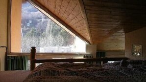 A bedroom with a wooden ceiling, a large window, and a bed with patterned bedding. - Serre-chevalier 1200, briançon, light runway, comfort, amenities  (Briançon)