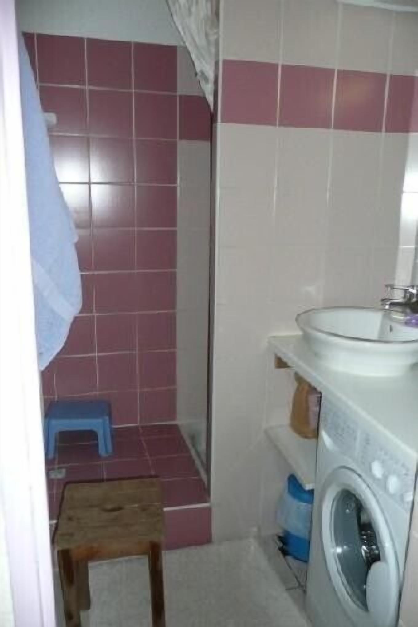 Bany compacte amb rentadora, un bany i un tamboret blau.