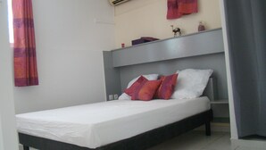 Uma cama de solteiro com roupa de cama branca e duas almofadas vermelhas e brancas.
