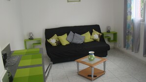 Sala de estar com sofá preto, mesinhas laterais verdes e uma pequena mesa de madeira com um vaso.