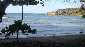 A beach with clear water, a rocky cliff, and sparse vegetation. - RENTAL T2 FURNITURE FOR VACANCY (Le Gosier)