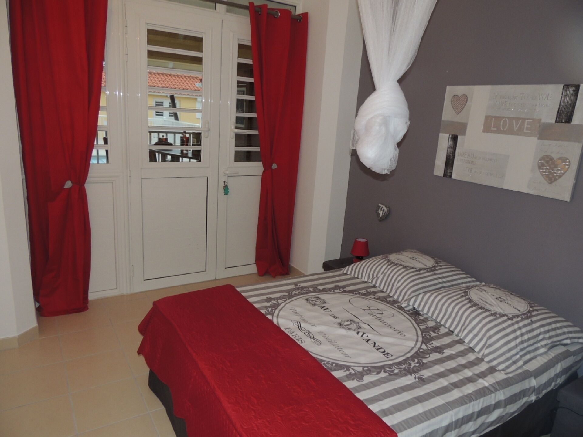Une chambre à coucher avec un lit, des rideaux rouges, un baldaquin blanc et un mur décoré de différents objets.