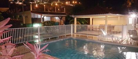 A swimming pool with a white fence, surrounded by potted plants.