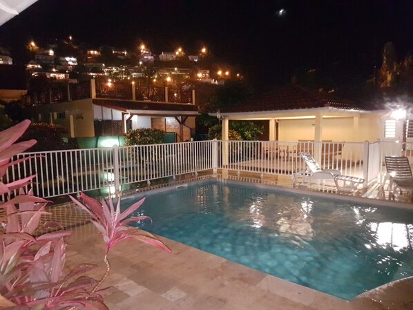 A swimming pool with a white fence, surrounded by potted plants.