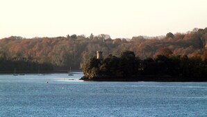 A coastal scene with a lighthouse on a small island, surrounded by water and trees.
