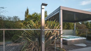 Un área moderna de hidromasaje al aire libre con cerramiento de vidrio, rodeada de plantas tropicales.