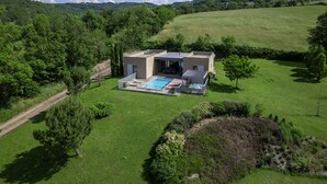 Una casa moderna con piscina, rodeada de exuberante vegetación y colinas.