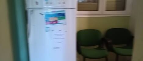 A kitchen with a white refrigerator, two green chairs, and a window with blinds.