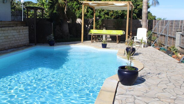 Ein Swimmingpool mit einer Pergola und Stühlen, umgeben von Kübelpflanzen und einer Steinterrasse.