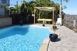 Une piscine agrémentée d’une pergola et de chaises, entourée de plantes en pot et d’une terrasse en pierre.