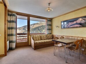 Una habitación con un banco de madera, una mesa de comedor con sillas, un ventanal con cortinas y vistas a la montaña.