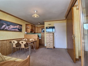 A compact kitchen with wooden cabinets, a dining area with a table and chairs, a ceiling light, and a door leading to another room.