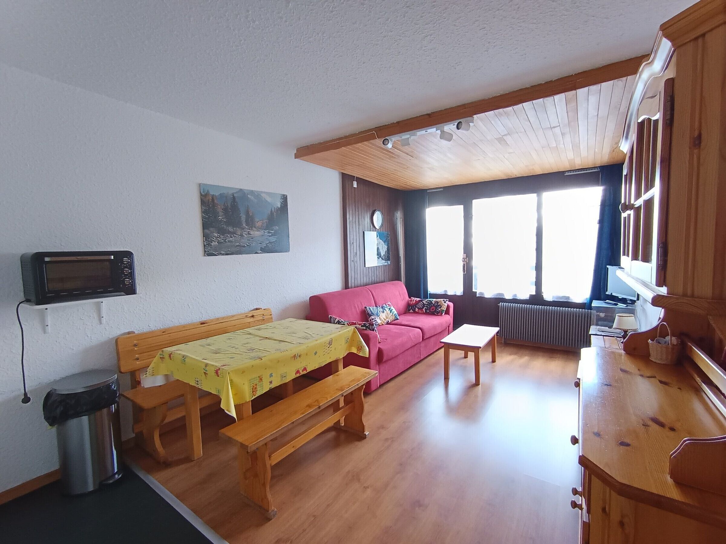 A cozy room with a wooden bench, a red sofa, a small table, and a radiator.