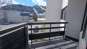 Varanda com vista para uma montanha nevada, área de estacionamento e edifícios ao fundo.