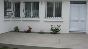 Un bâtiment doté de trois fenêtres, chacune ornée d’une grille métallique, d’une porte blanche et d’un petit jardin agrémenté de fleurs roses.