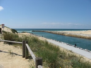 Une plage avec une promenade en bois, un panneau indicateur et une digue rocheuse.