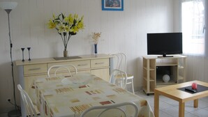Une pièce comprenant une table à manger, des chaises, un téléviseur posé sur un meuble, un vase avec des fleurs et une lampe.
