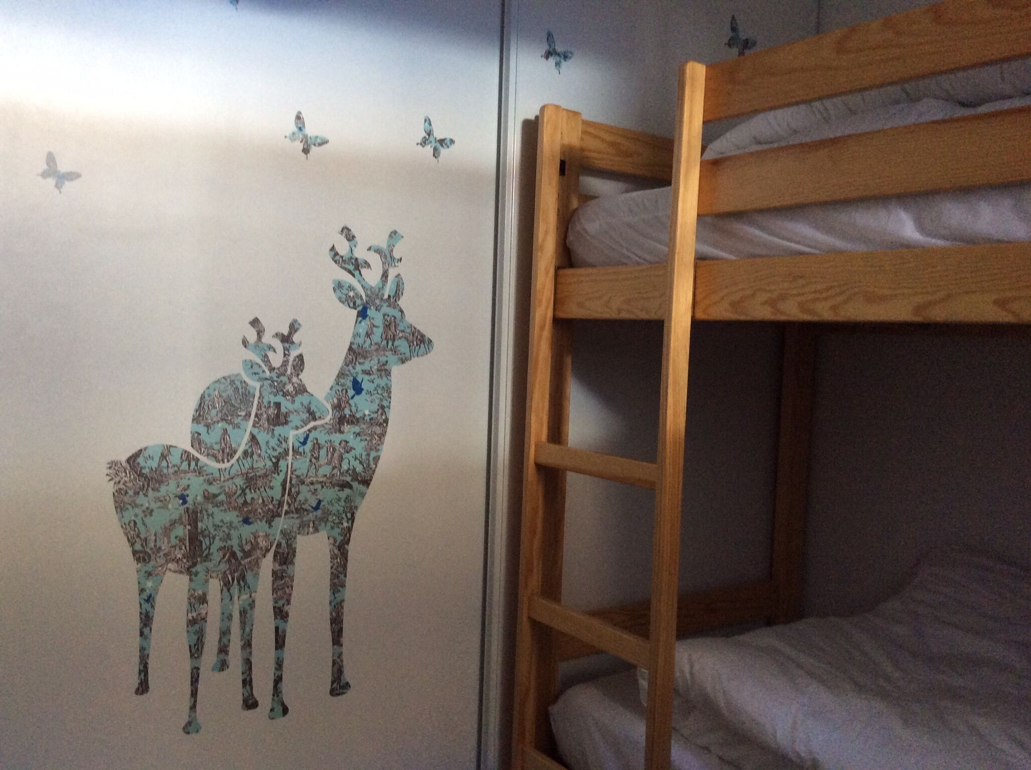 A bunk bed with a wall decal of deer and butterflies.