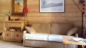 A cozy room with a wooden log wall, a beige sofa, a wooden side table, a mirror, and a framed picture of a snowy landscape. - Serre Chevalier Le Mônétier Les Bains F3 Magnifique vue face aux Ecrins (Le Monêtier-Les-Bains)