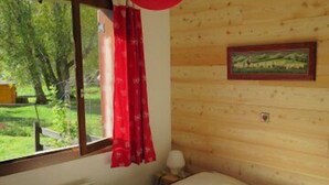 A bedroom with a bed, a window with a view of greenery, a red hanging light, and a framed picture on the wall. - Serre Chevalier Le Mônétier Les Bains F3 Magnifique vue face aux Ecrins (Le Monêtier-Les-Bains)