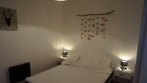 Une chambre à coucher comprenant un lit, deux tables de chevet avec des lampes, un élément décoratif fixé au mur et un radiateur.