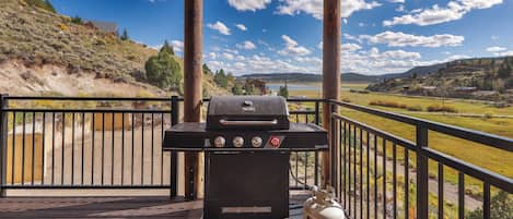 Una parrilla de barbacoa en una terraza de madera con vistas panorámicas a colinas y un lago.