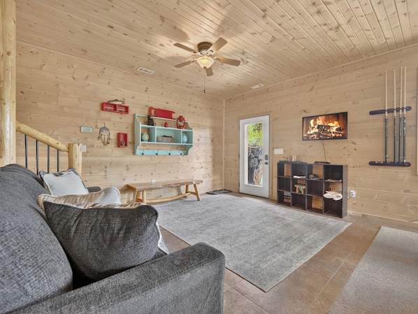 A cozy room with a wooden ceiling, a bench, a sofa, a fireplace, and a television.