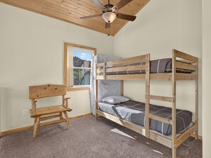 A bunk bed room with a ceiling fan, a window with a view, and a wooden bench.