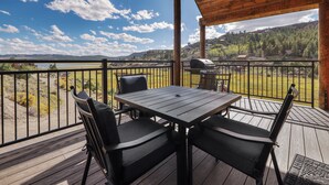 A wooden deck with a table and chairs, overlooking a lake and hills.