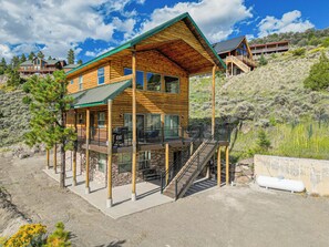 A wooden cabin with a balcony, a staircase, and a view of the surrounding landscape.