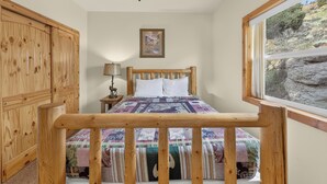 A bedroom with a wooden bed, a nightstand with a lamp, a wooden wardrobe, a ceiling fan, and a window with a view of the outdoors.
