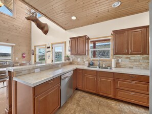 A modern kitchen with wooden cabinets, a stainless steel dishwasher, and a large window overlooking a scenic landscape.