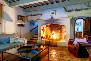 A cozy living room with a fireplace, a sofa, a leather armchair, and a glass coffee table.