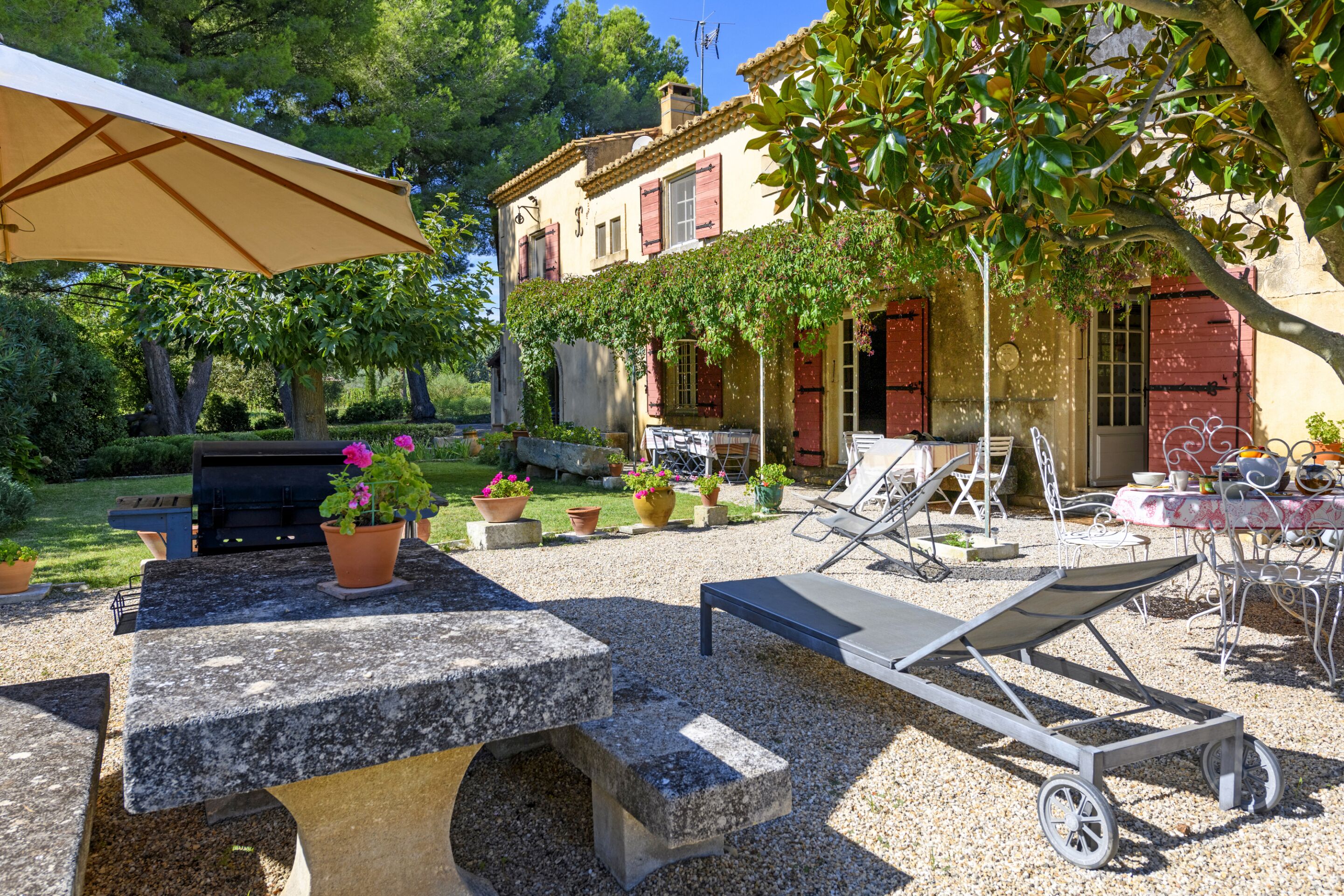 A patio with a grill, lounge chairs, and a table with potted plants.
