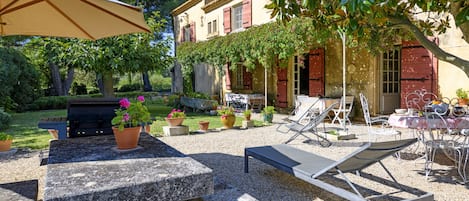 A patio with a grill, lounge chairs, and a table with potted plants.