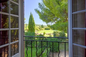 Blick aus einem Fenster mit Metallgeländer auf einen gepflegten Garten mit einem hohen Baum, einem Picknicktisch und einer Rasenfläche.
