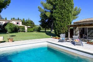 A swimming pool with lounge chairs and a sunbed, surrounded by a well-maintained lawn and trees.