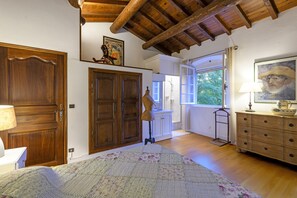 A bedroom with wooden doors, a large bed, a dresser, and a window with curtains. - Mas de la Treille - pool - garden (Les Baux-De-Provence)